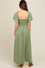woman wearing a green maternity maxi dress with a smocked bodice and flutter sleeves, view from the back
