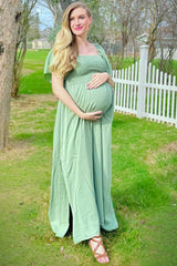 woman wearing a light green maternity maxi dress and holding her baby bump in a grassy outdoor setting