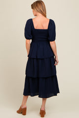 woman wearing a navy blue maternity tiered dress with puff sleeves and a smocked bodice, viewed from the back