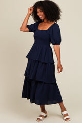 woman wearing a navy blue tiered midi dress with puff sleeves and a square neckline, styled with white sandals