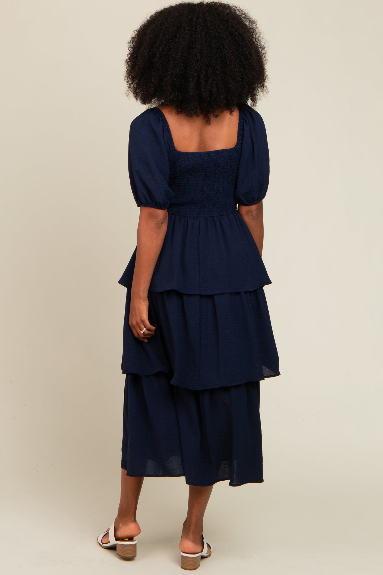 woman wearing a navy blue tiered dress with puff sleeves, standing with her back to the camera