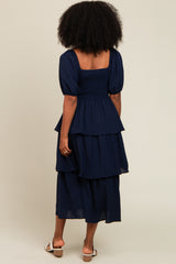 woman wearing a navy blue tiered dress with puff sleeves, standing with her back to the camera