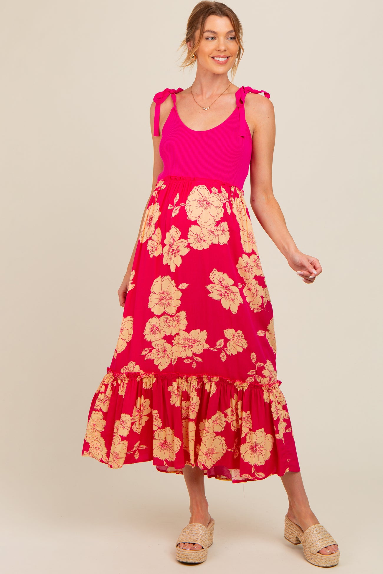 woman wearing a pink floral maternity maxi dress with ruffle details and tie straps, showcasing her baby bump