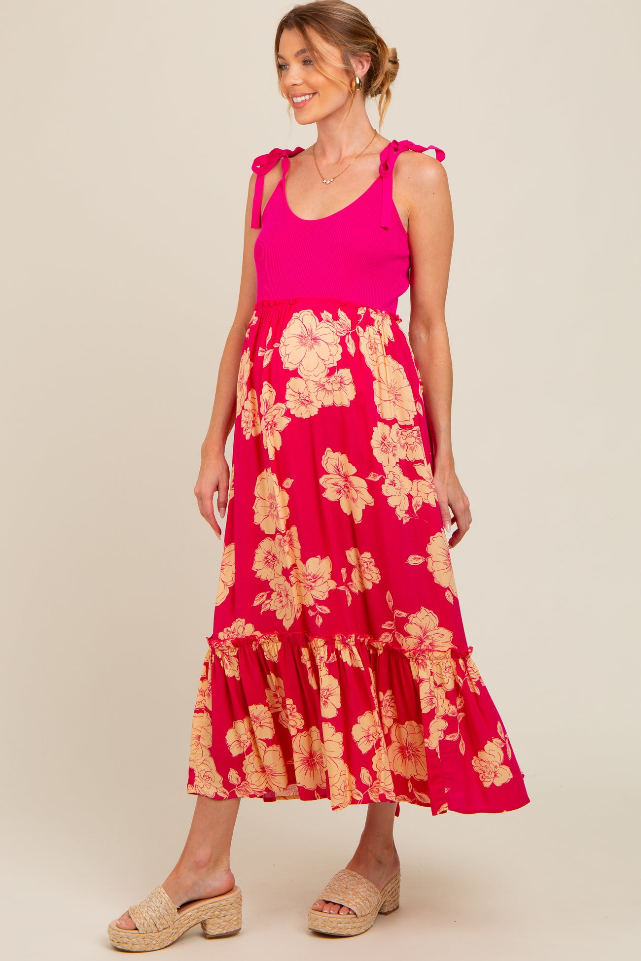 woman wearing a pink floral maternity maxi dress with ruffled hem and tie straps, showing a baby bump