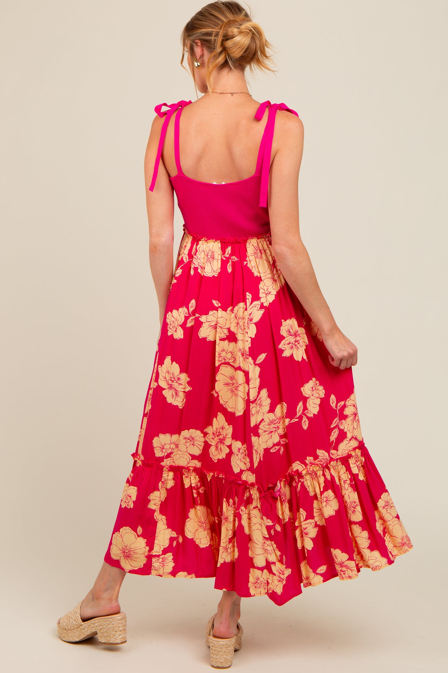 woman wearing a pink floral maternity dress with tie straps and a ruffled hem, showing her back