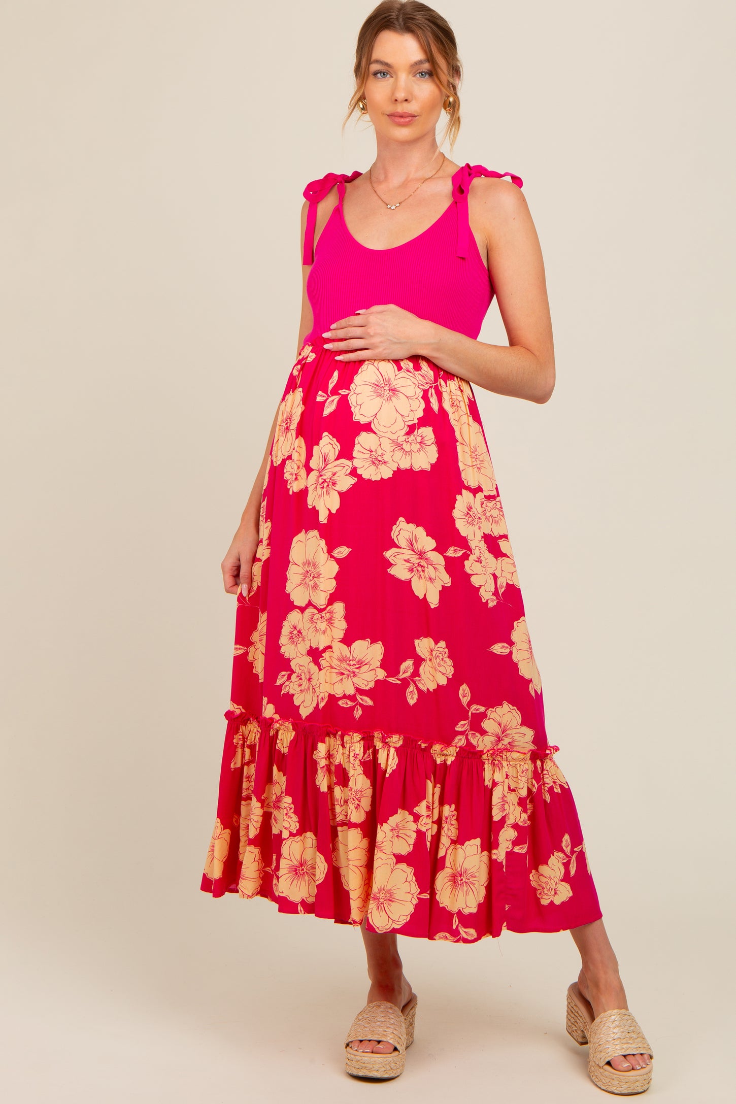 woman wearing a pink maternity maxi dress with floral print and ruffle hem, holding her baby bump