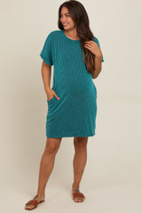 woman wearing a teal striped maternity dress with short sleeves and pockets, standing in a relaxed pose