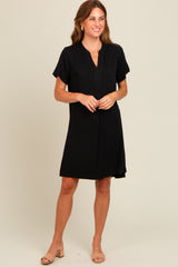 woman wearing a black short sleeve shift dress with a v-neck and button detail, styled with nude sandals