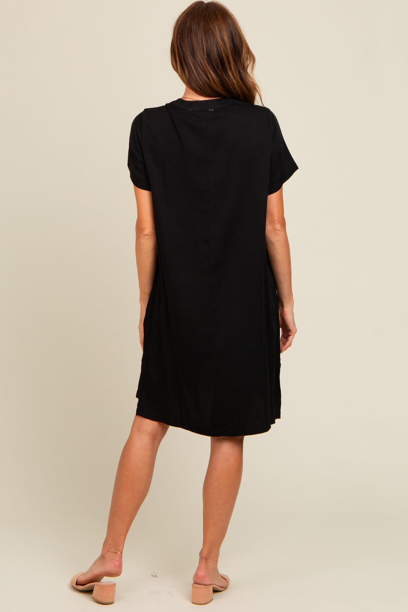 woman wearing a black short sleeve dress, viewed from the back, with a slightly loose fit and above the knee length