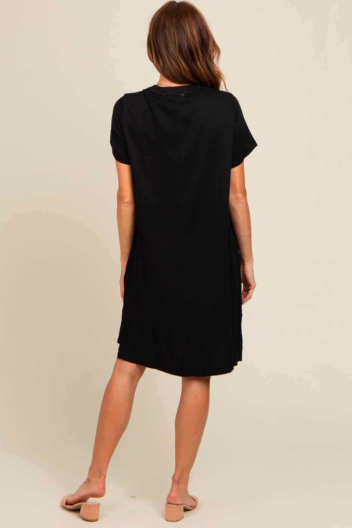 woman wearing a black short sleeve dress, viewed from the back, with a slightly loose fit and above the knee length