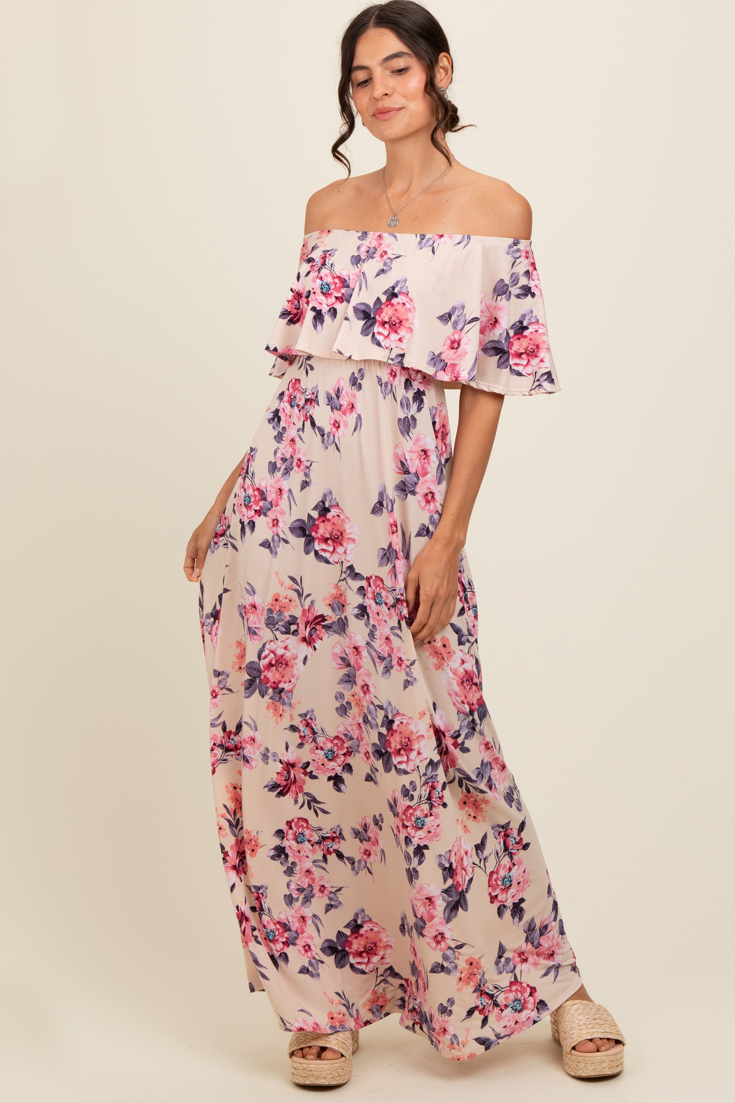 woman wearing a floral off-the-shoulder maxi dress with a ruffled layer and a light pink background