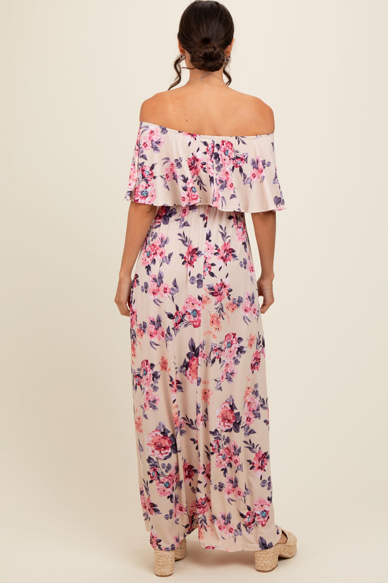 woman wearing a floral off-the-shoulder maxi dress with ruffle detail, showing the back view with a light beige background