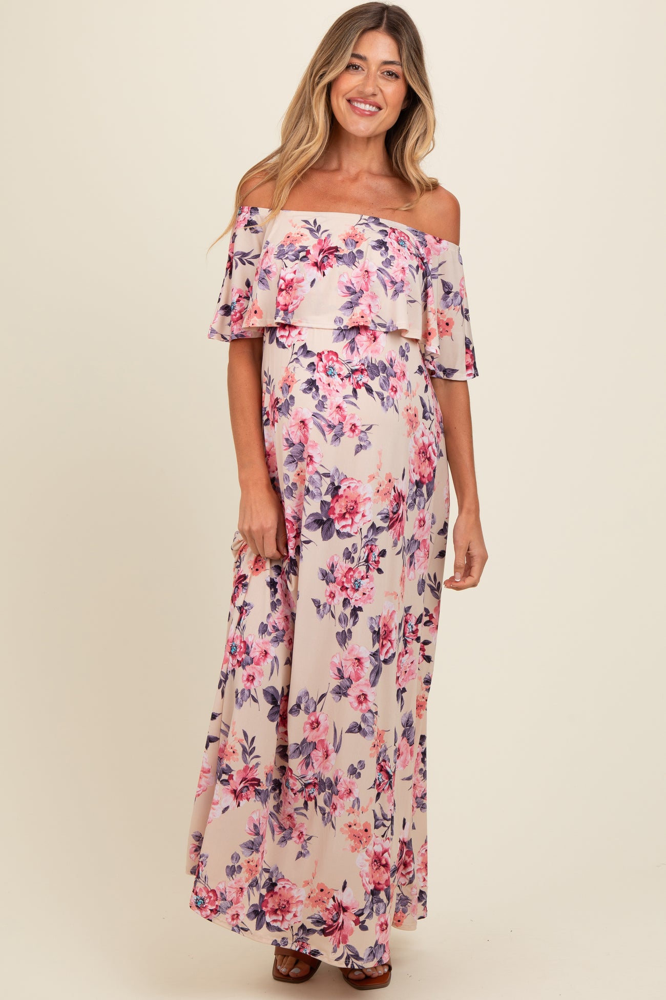 woman wearing a floral off-shoulder maxi maternity dress with a flowy design and a visible baby bump