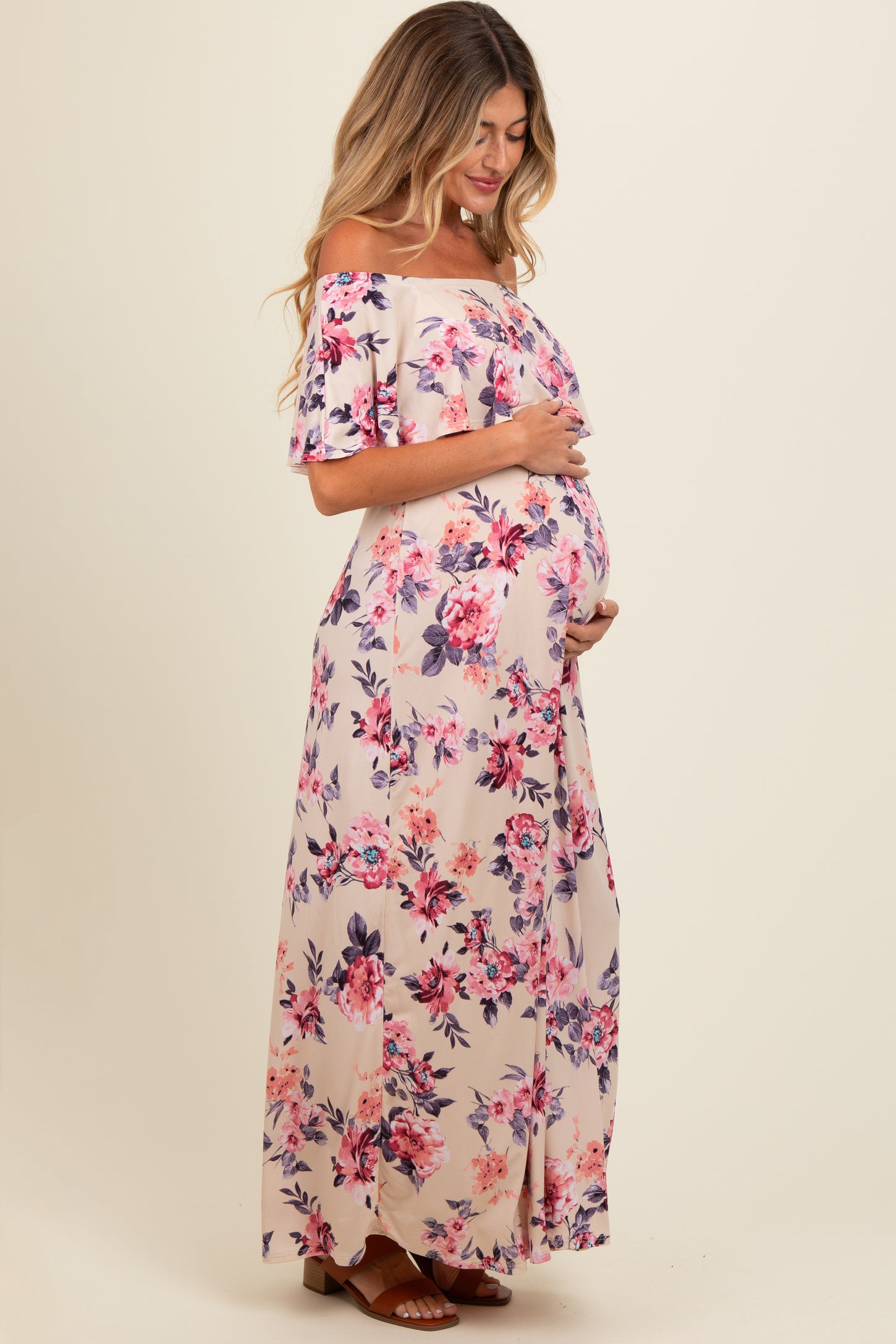 woman wearing a floral off-the-shoulder maternity maxi dress and cradling her baby bump