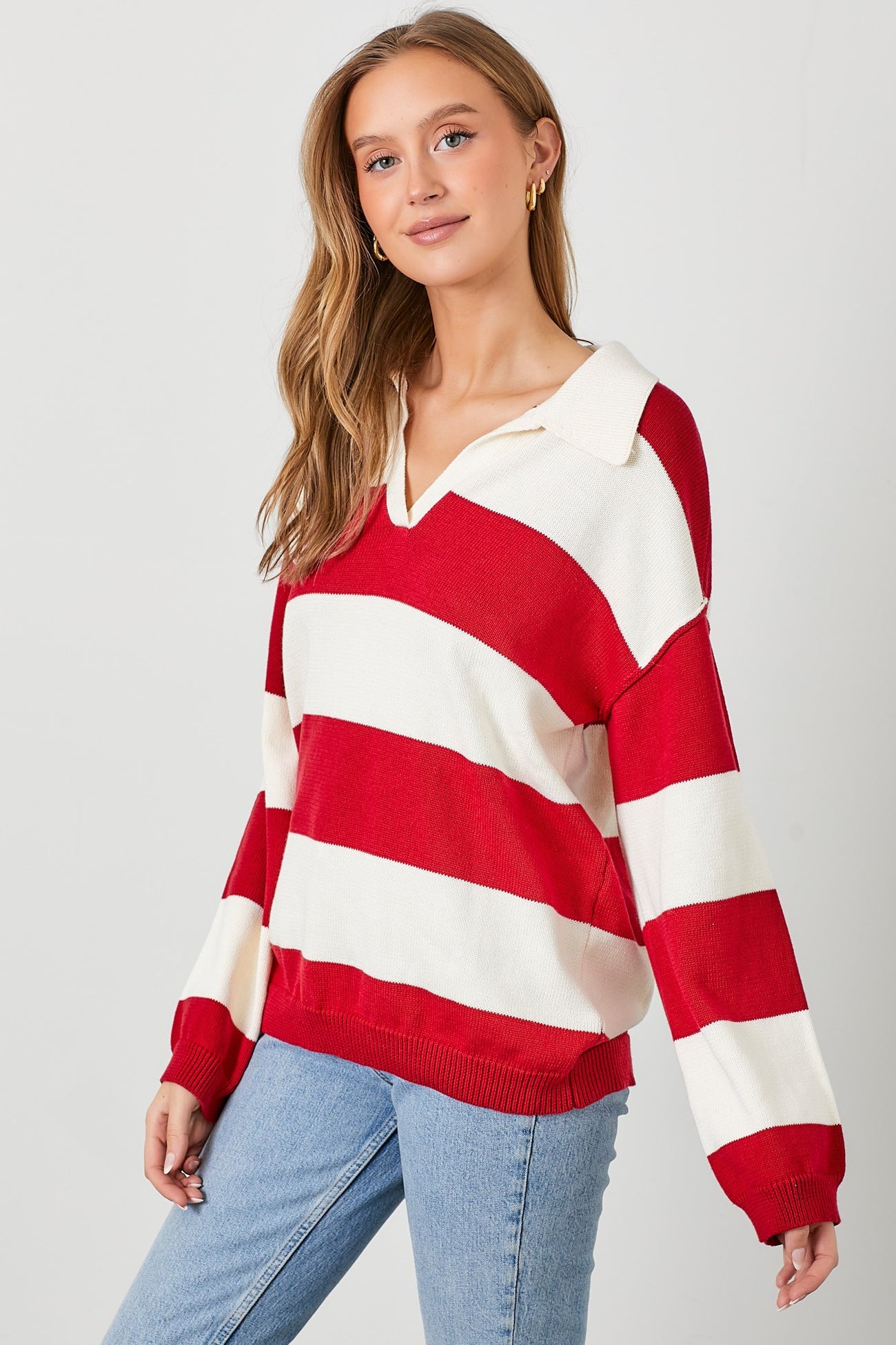 woman wearing a red and white striped oversized v-neck sweater with a collar and light blue jeans