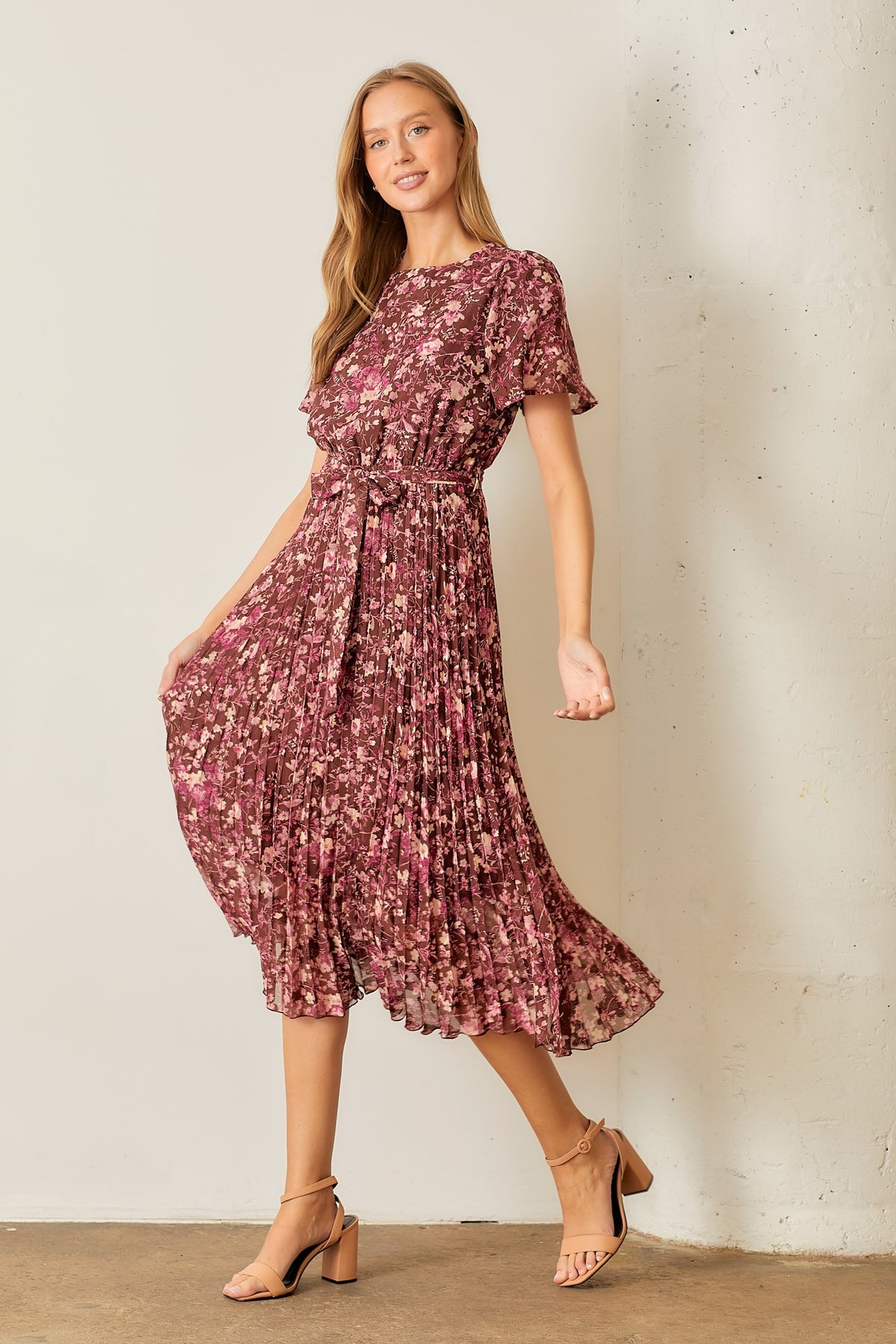 woman wearing a floral pleated midi dress in shades of pink with short sleeves and a tie waist detail