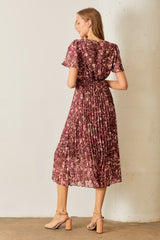 woman wearing a purple floral pleated midi dress, showing the back view with short sleeves and a cinched waist