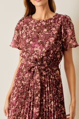 woman wearing a brown floral pleated dress with short puff sleeves and a belted waist