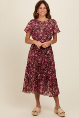 woman wearing a floral midi dress with short sleeves in shades of purple and pink, standing and smiling
