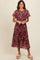 woman wearing a floral midi dress with short sleeves in shades of purple and pink, standing and smiling