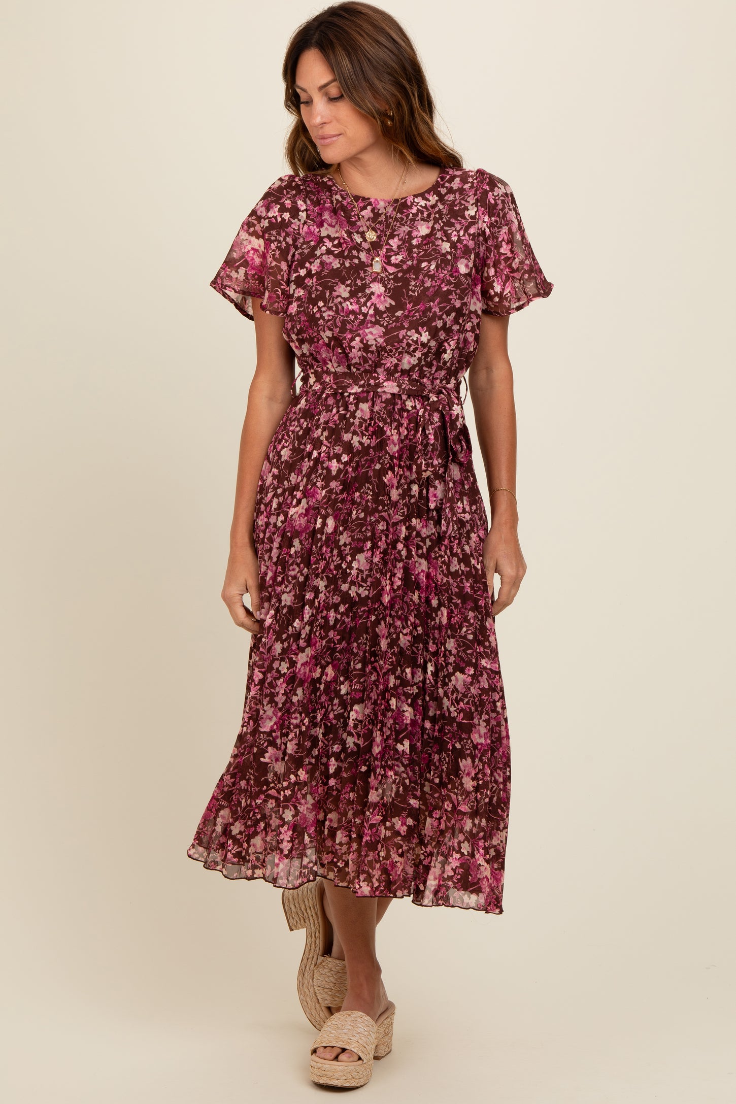 woman wearing a burgundy floral midi dress with short sleeves and a tie waist, standing and smiling