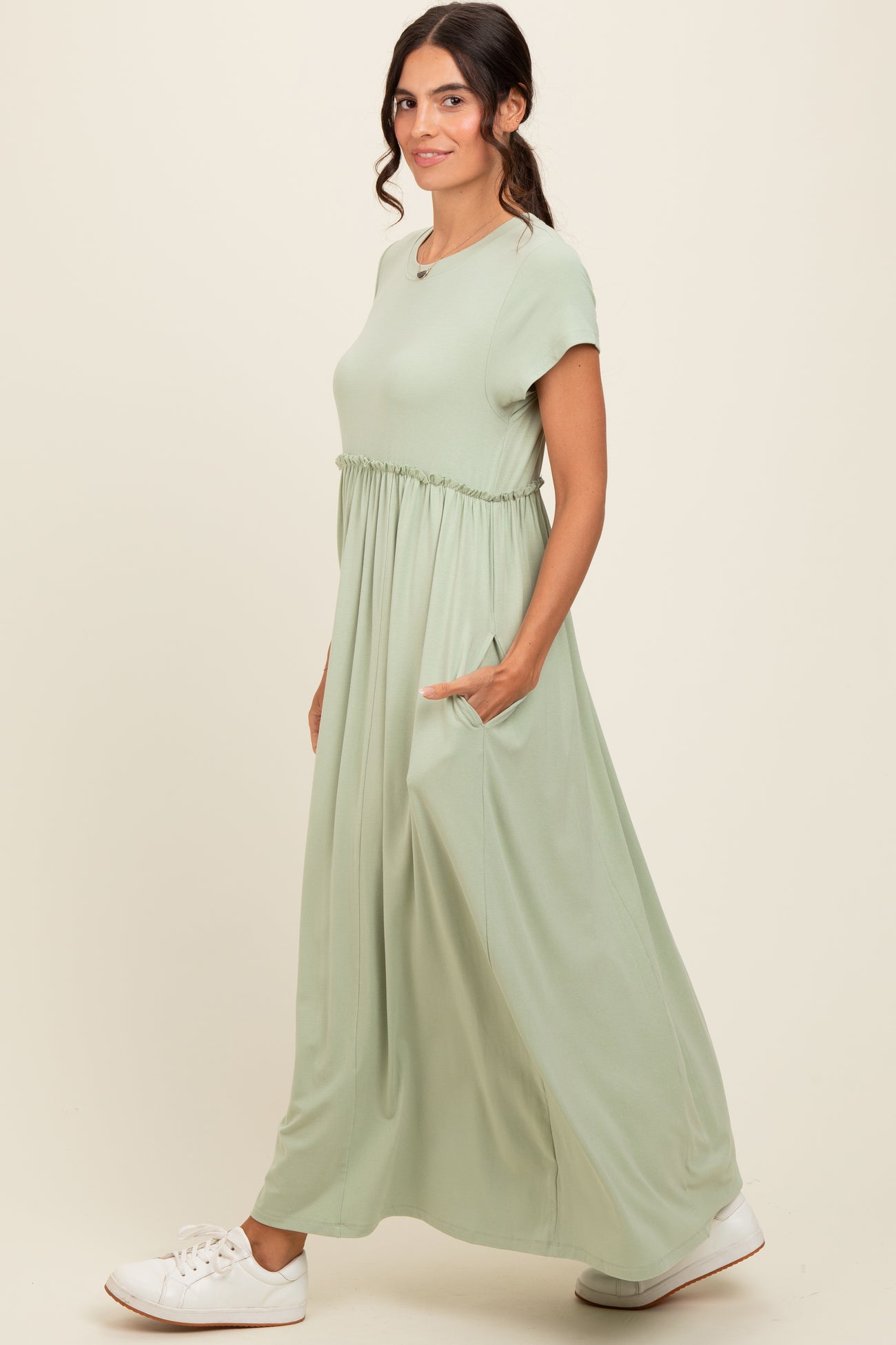 woman wearing a light green maxi dress with short sleeves and side pockets, standing in profile with a casual look
