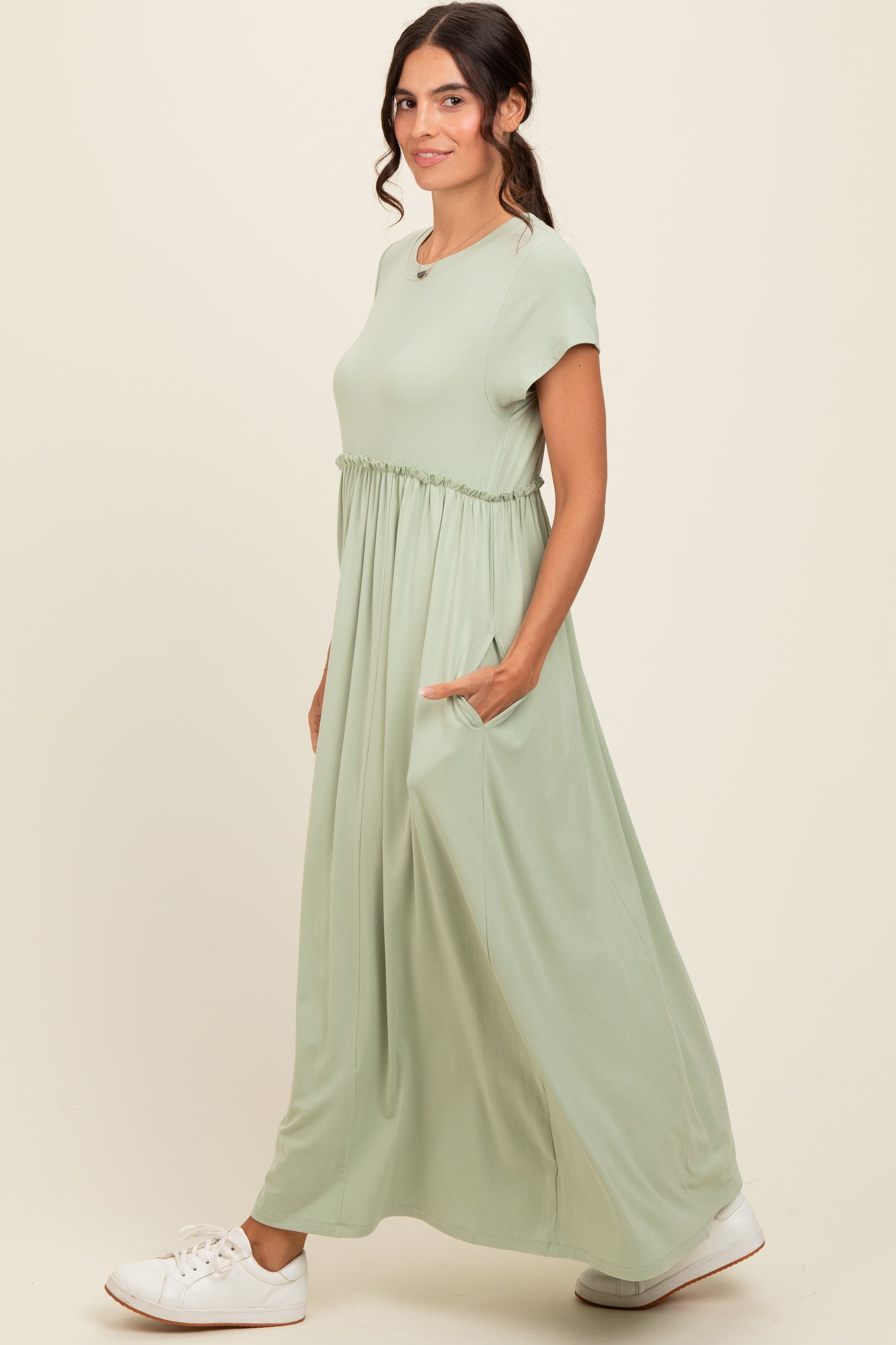 woman wearing a light green maxi dress with short sleeves and side pockets, standing in profile with a casual look