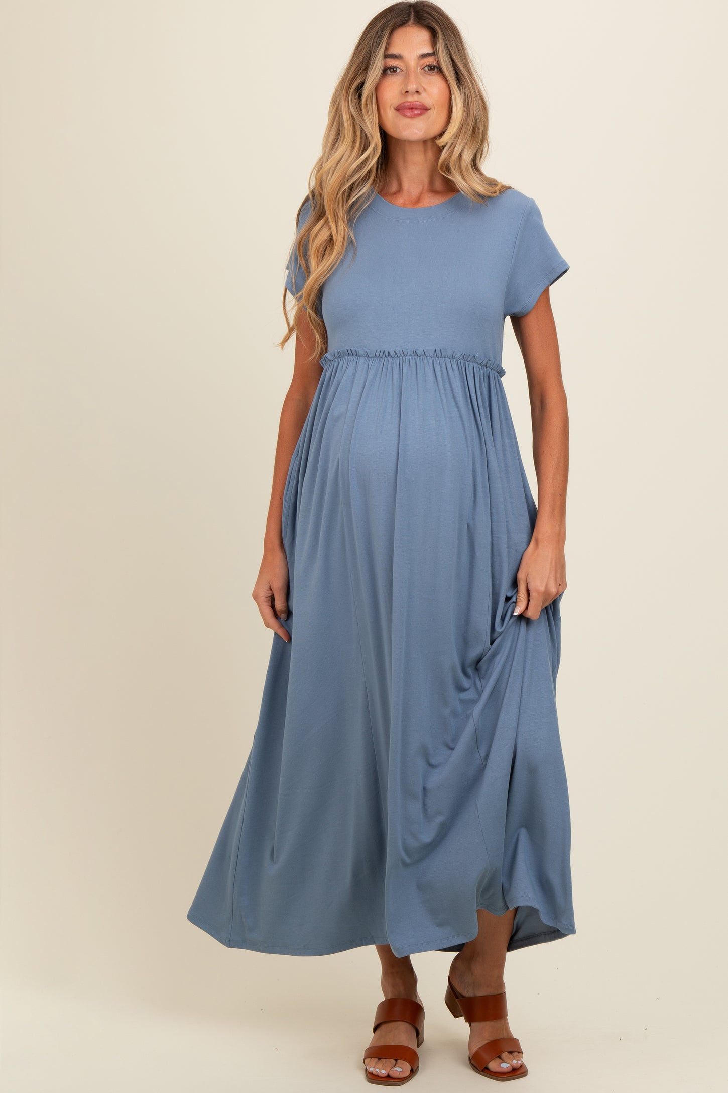 woman wearing a blue short sleeve maternity dress with a gathered waist and a flowing skirt, showing her baby bump