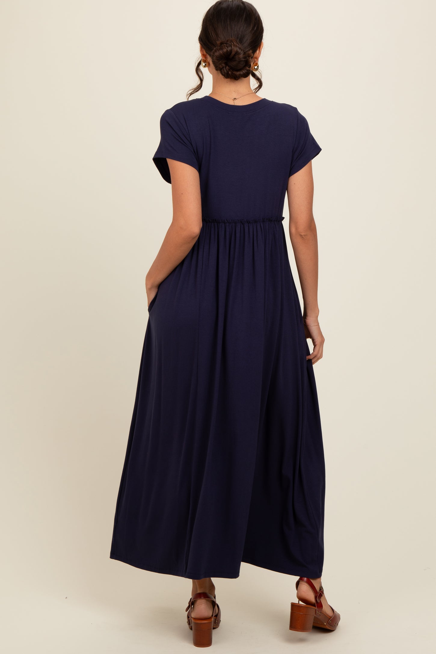 woman wearing a navy blue maxi dress with short sleeves and a gathered waist, standing with her back to the camera