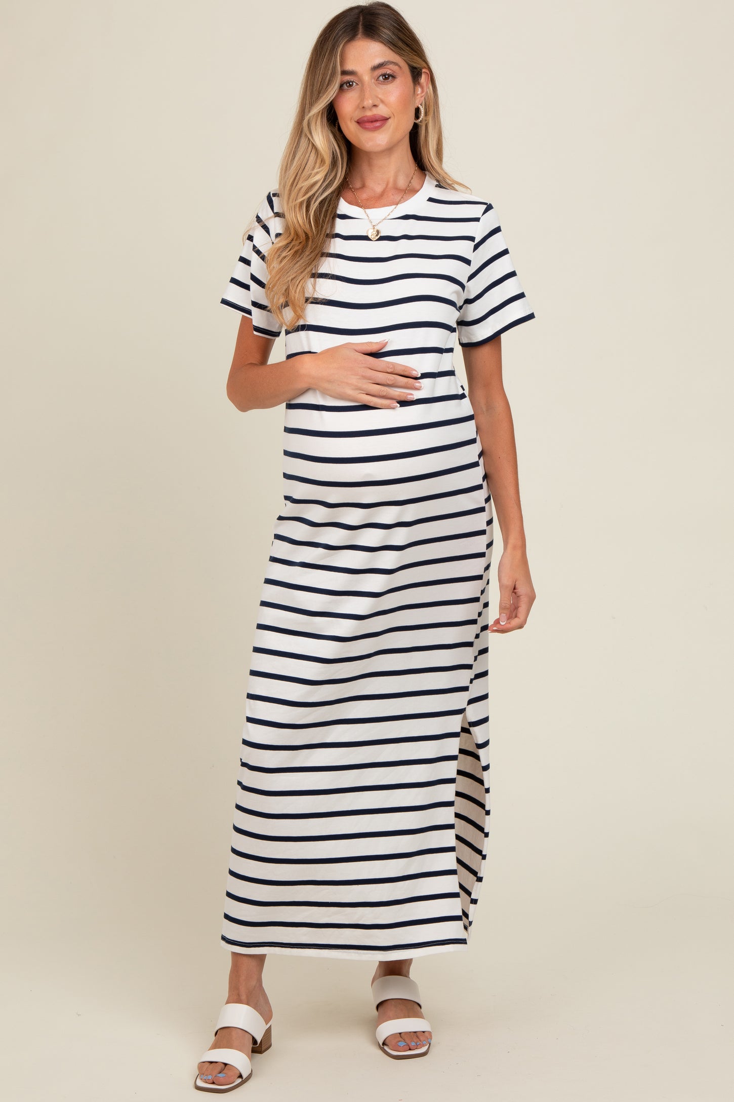 woman wearing a striped maternity maxi dress with short sleeves and a side slit, cradling her baby bump