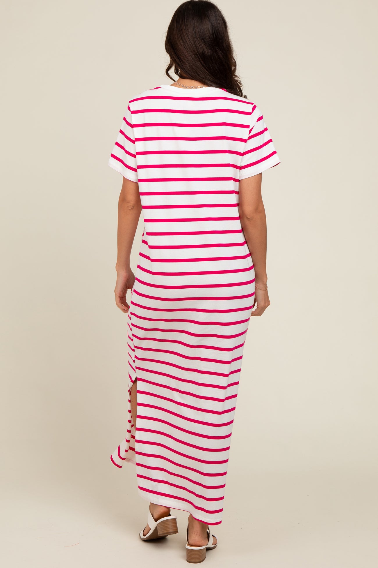woman wearing a white and pink striped maxi dress with short sleeves and a side slit, seen from the back
