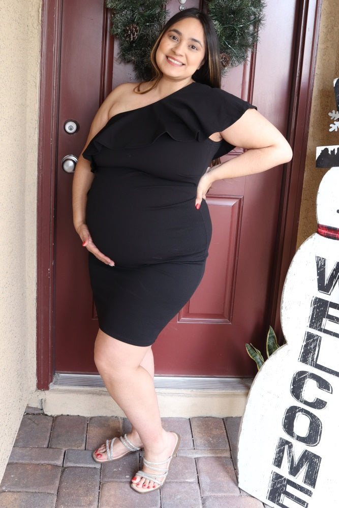 woman wearing a black one-shoulder maternity dress with ruffles and holding her baby bump