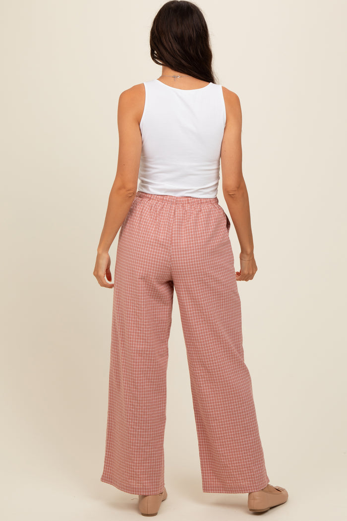 woman wearing a white sleeveless tank top and pink checked wide-leg pants, facing away from the camera