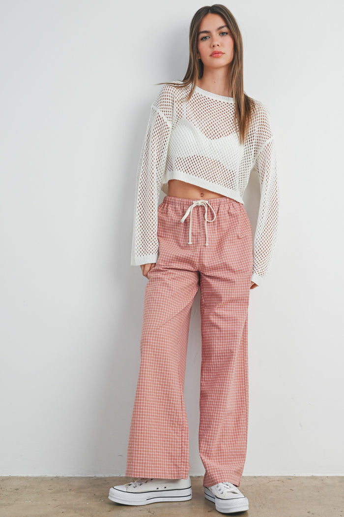 woman wearing a white mesh long sleeve crop top and pink checkered wide-leg pants with a drawstring