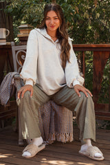 woman wearing a light gray maternity pullover with sleeves and green checkered maternity pants, sitting on a porch