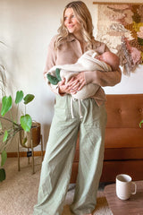 woman wearing a beige oversized knit sweater and green checkered wide-leg pants while holding a baby
