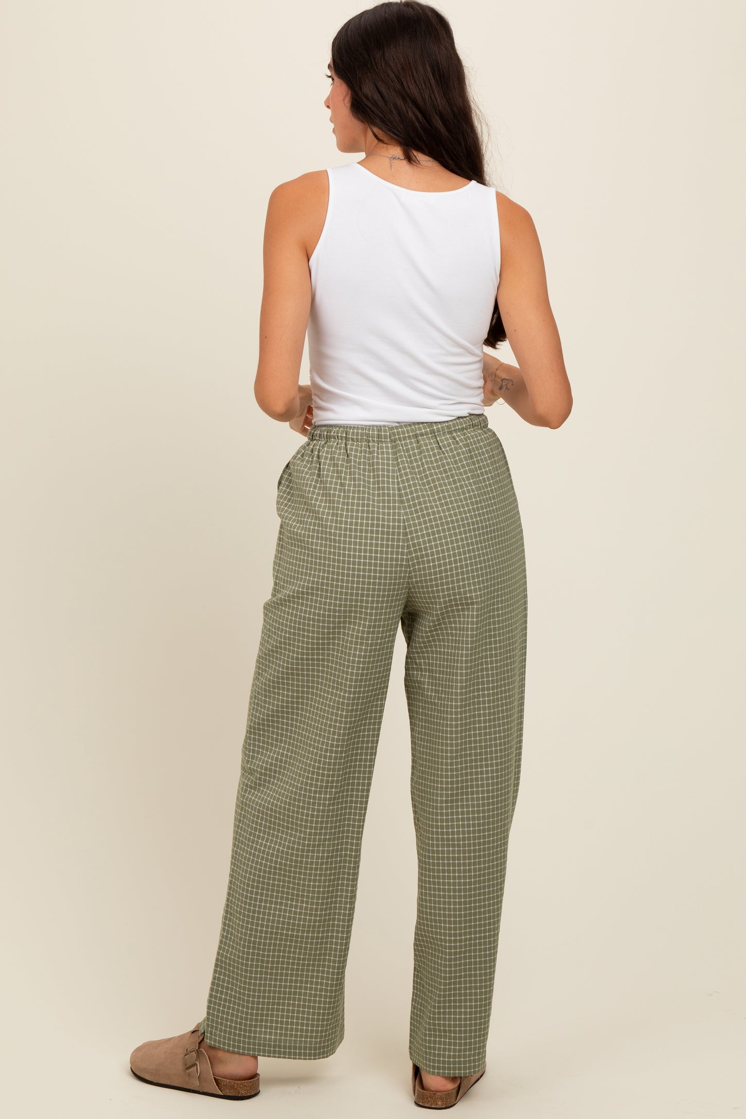 woman wearing a white tank top and green checkered wide-leg pants, viewed from the back