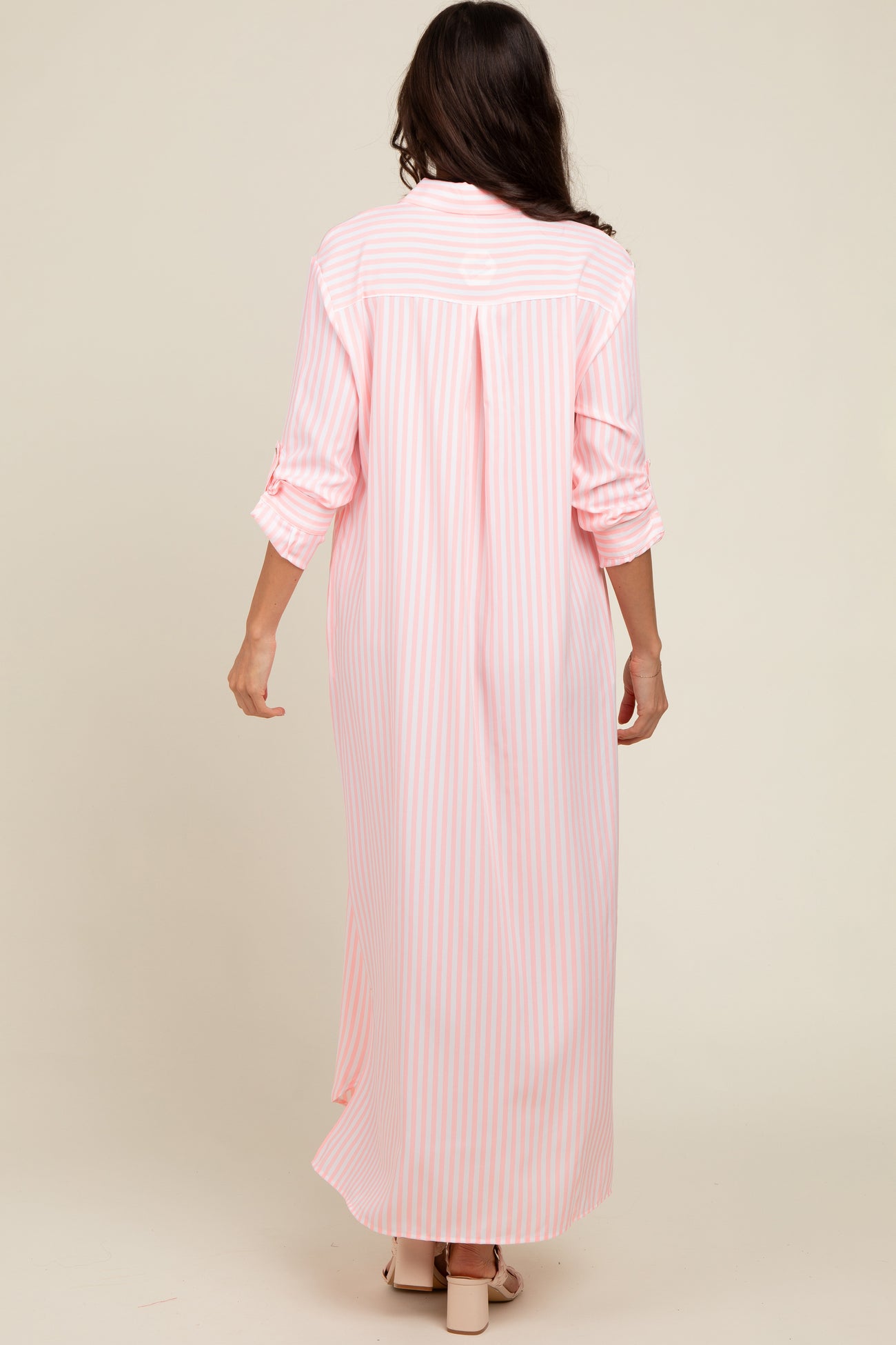 woman wearing a long pink and white striped maxi dress with rolled-up sleeves, seen from the back