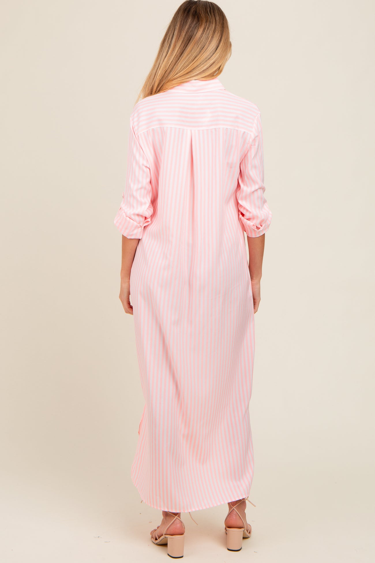woman wearing a pink and white striped maternity maxi dress, showing the back view with long sleeves rolled up