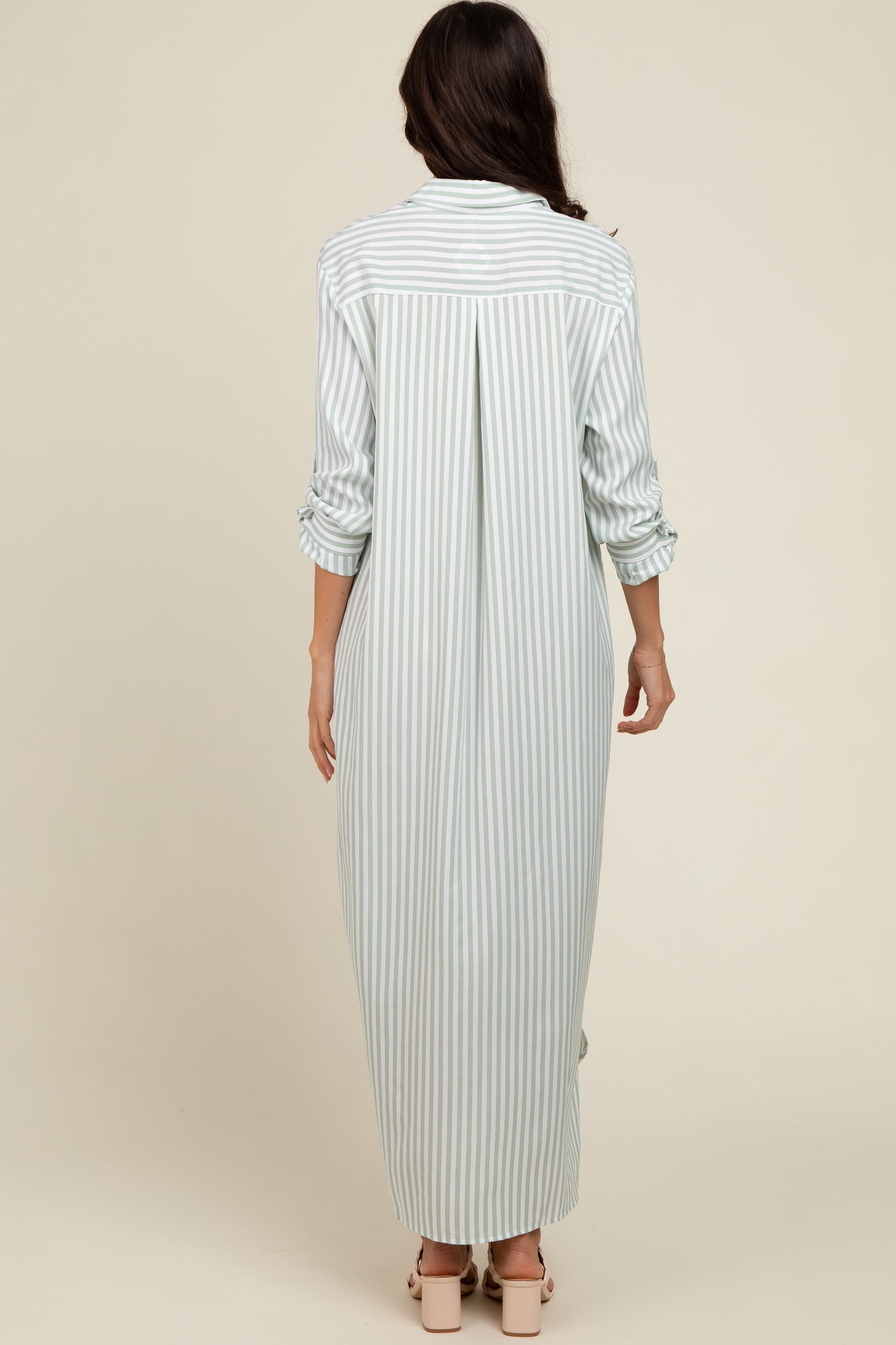 woman wearing a long striped button-up dress with rolled sleeves, showing the back view in light green and white stripes