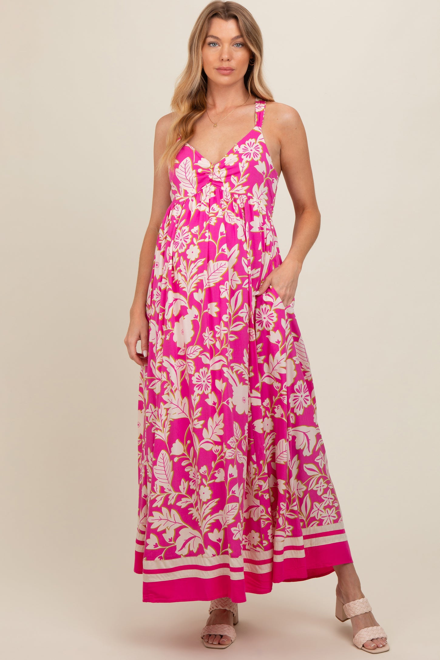 woman wearing a pink floral maxi maternity dress with a v-neck and pockets, featuring a flowy silhouette and adjustable straps