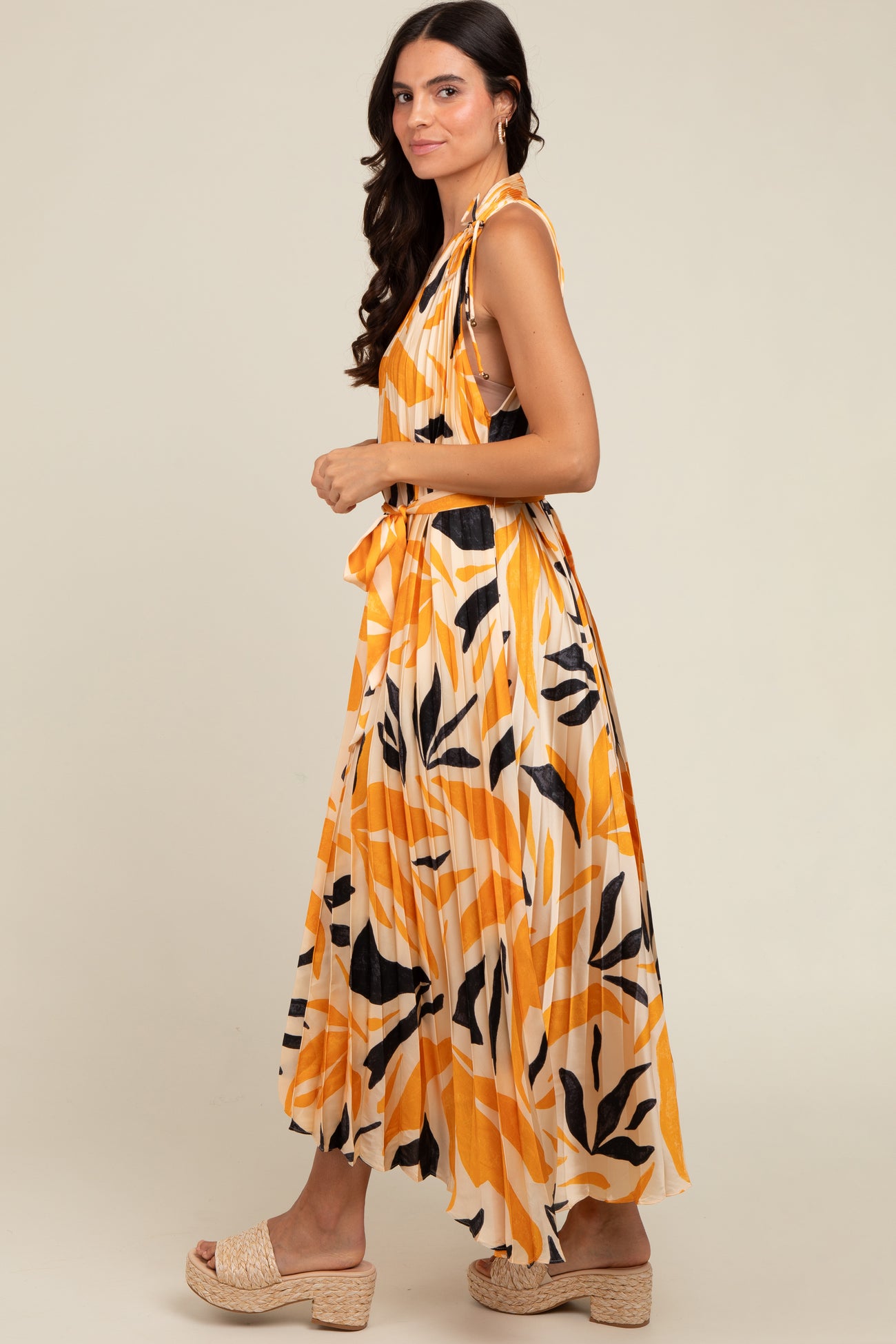 woman wearing an orange and white maxi dress with abstract leaf patterns and a tied detail at the shoulder