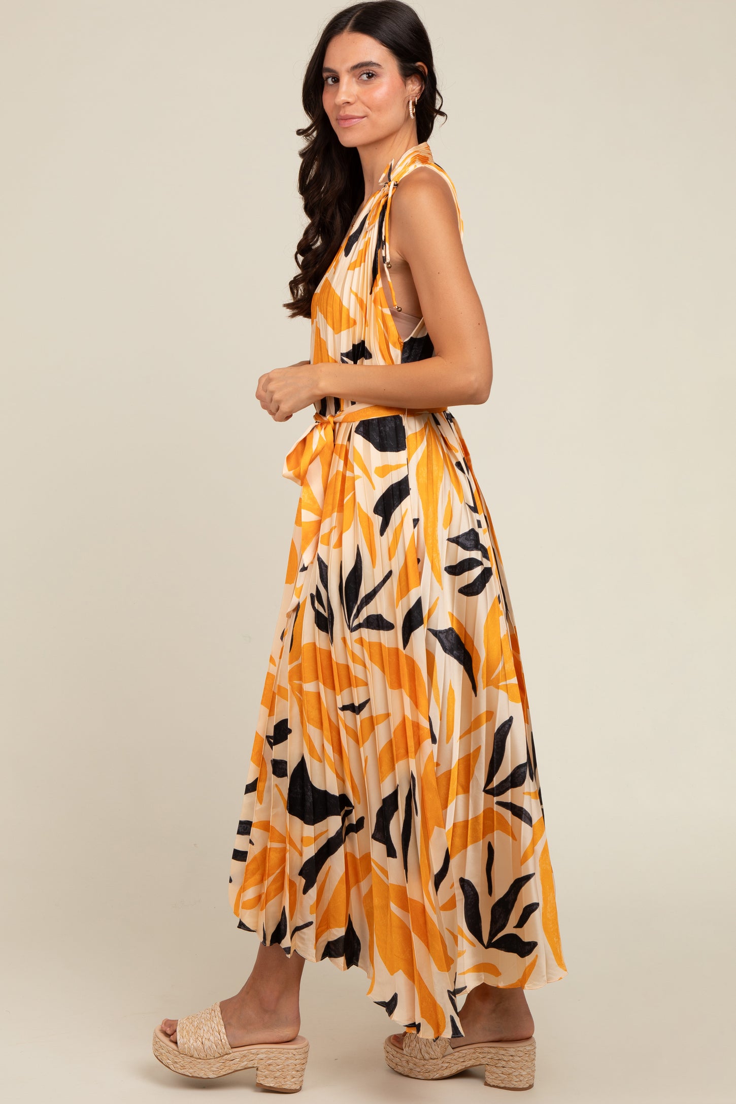 woman wearing an orange and white maxi dress with abstract leaf patterns and a tied detail at the shoulder