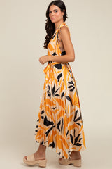 woman wearing an orange and white maxi dress with abstract leaf patterns and a tied detail at the shoulder