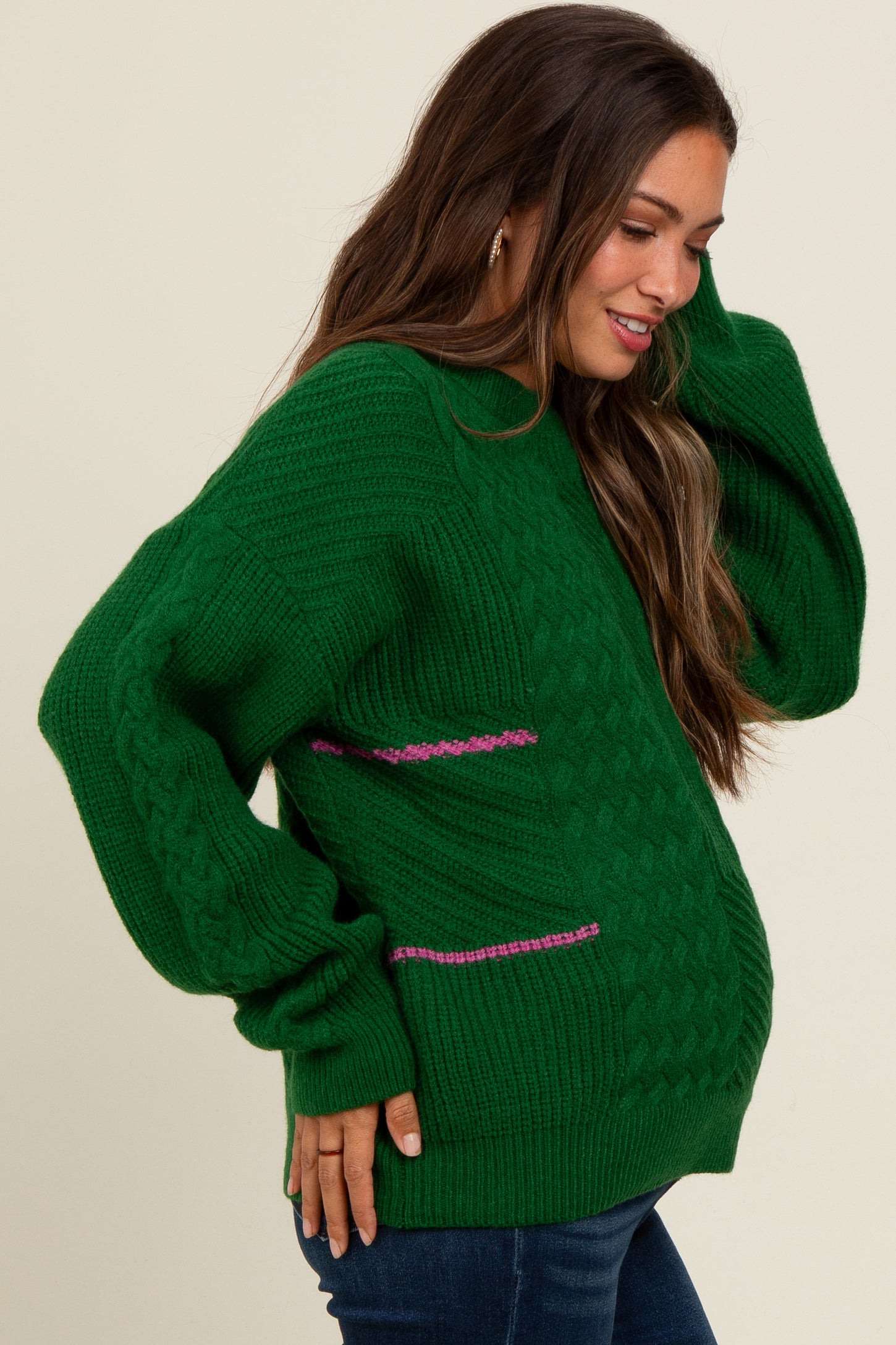 woman wearing a green cable knit maternity sweater with pink stripe details and a visible baby bump