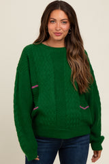 woman wearing a green oversized knit maternity sweater with pink accents and denim jeans