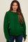 woman wearing a green oversized knit maternity sweater with pink accents and denim jeans
