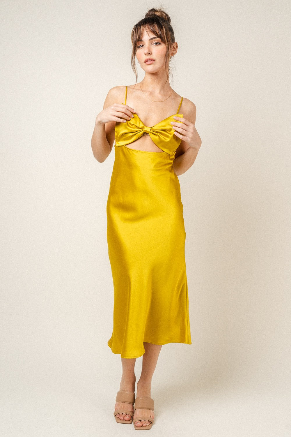 woman wearing a yellow satin midi dress with a bow detail and spaghetti straps
