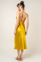 woman wearing a backless mustard yellow satin slip dress, showing a smooth silhouette and knee-length hem