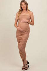 woman wearing a beige strapless maternity dress with ruched detailing and holding her baby bump
